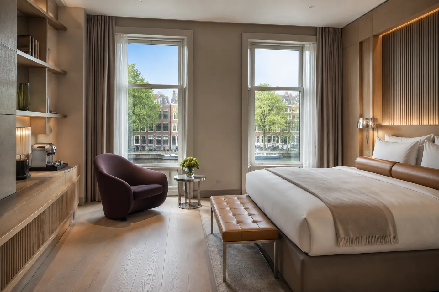 Suite met linnen bed, hoge ramen en een aubergine fauteuil
